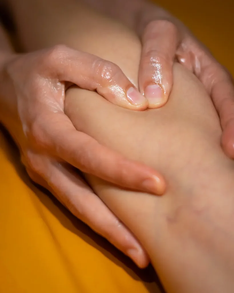 Farbfoto Kalari Massage. Hände massieren Bein