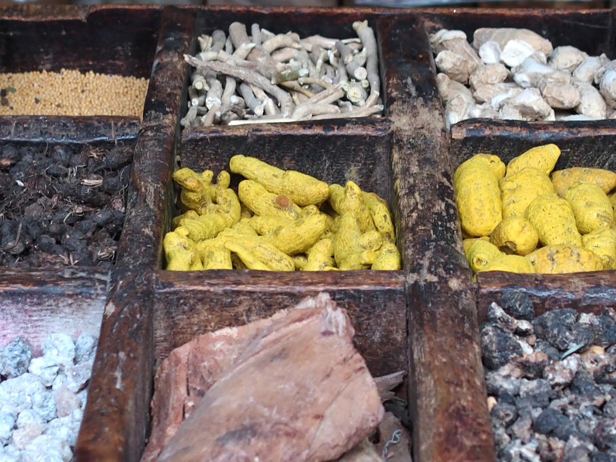 Ayurveda. Farbfoto von sieben verschiedenen āyurvedischen Gewürzen, die offenen in einer alten Gewürzbox aus Holz liegen.